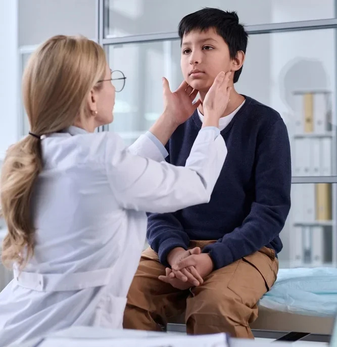 A Female Doctor In A White Coat Examining A Young Boy'S Neck/Throat.