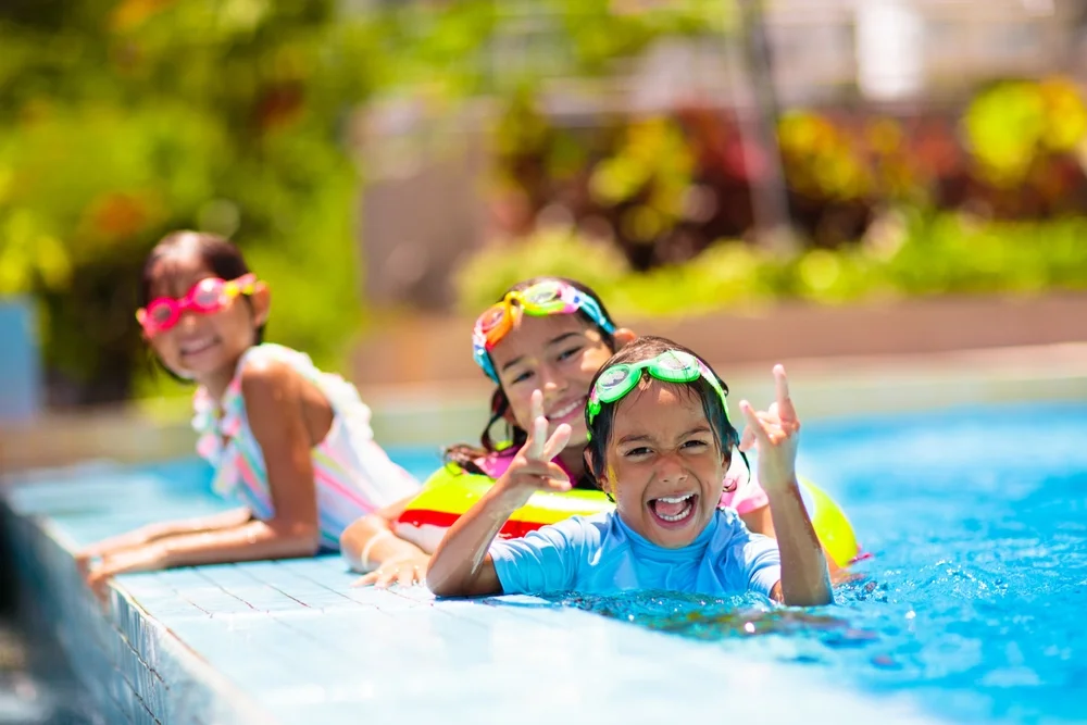 Child Swim Under Water. Kids Play In Swimming Pool. Children Learn To Swim In Outdoor Pool Of Tropical Resort During Family Summer Vacation. Water And Splash Fun For Young Kid On Holiday.