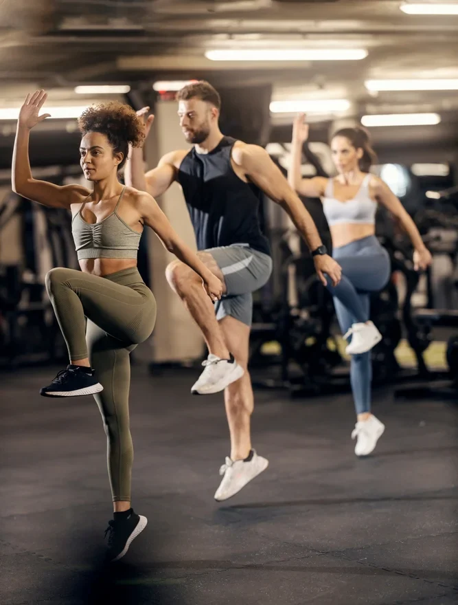 Three People In Athletic Wear Doing High-Knee Exercises In A Gym